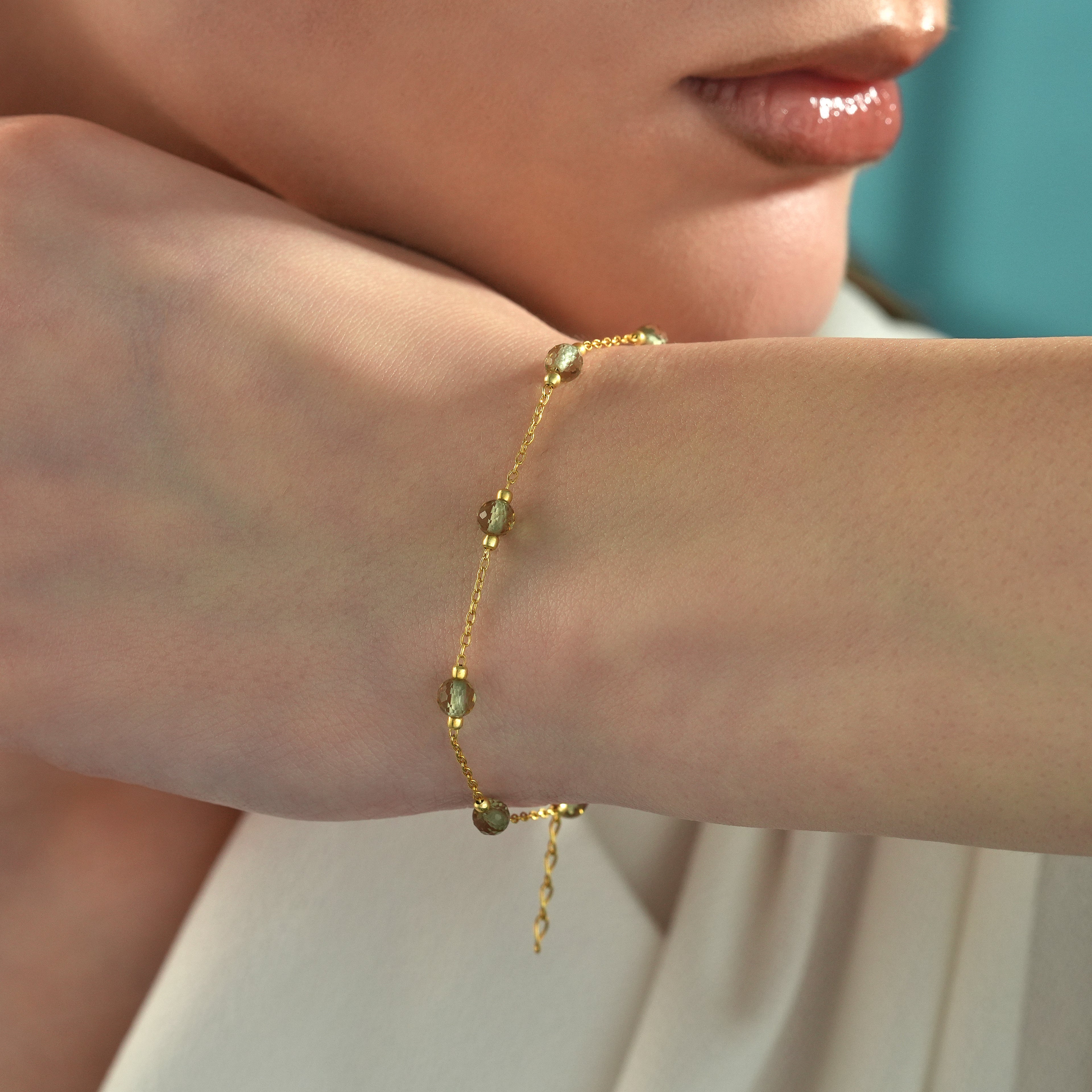 Close-up of a 14K gold plated bracelet with faceted color changing gemstones worn on a woman's wrist.