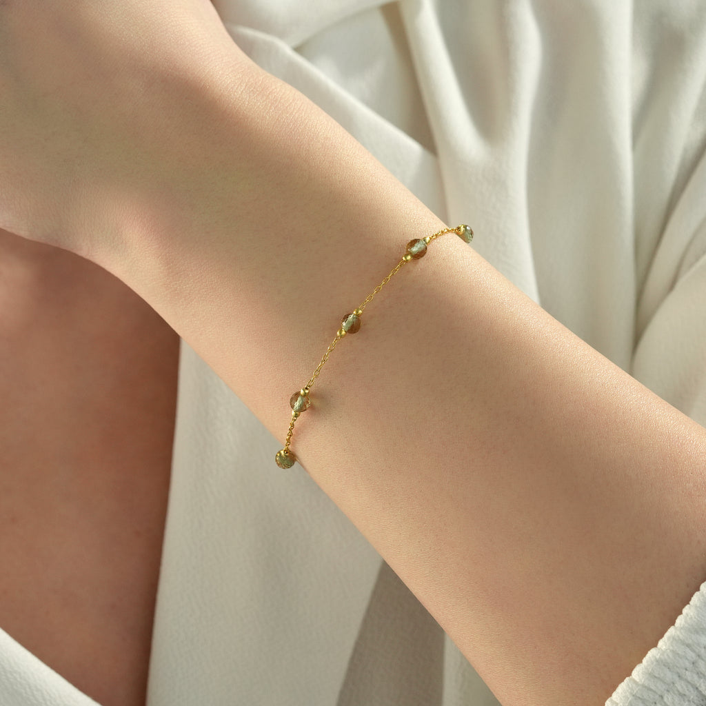Woman wearing a delicate 14K gold plated bracelet with faceted color changing gemstones and minimalist chain design.