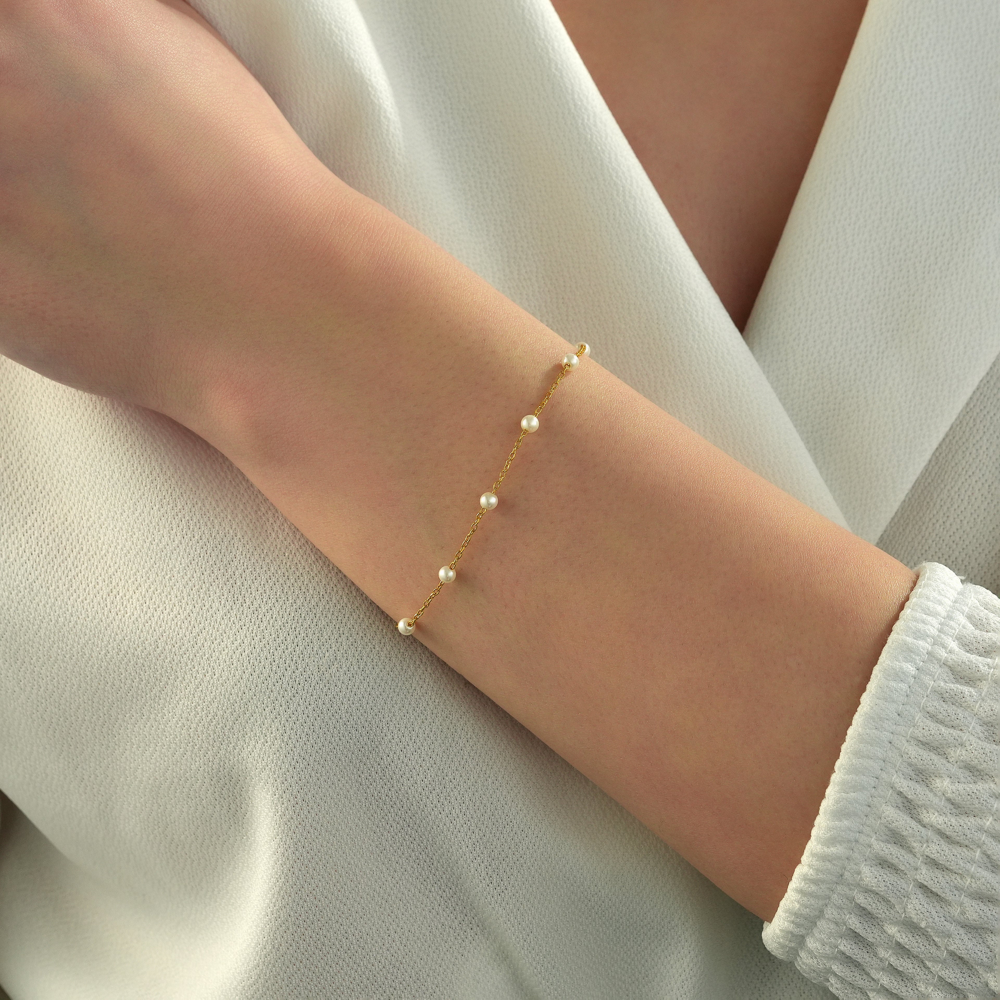 Delicate 14K gold plated 925 sterling silver pearl bracelet featuring evenly spaced white pearls on a fine chain, worn on a woman's wrist.
