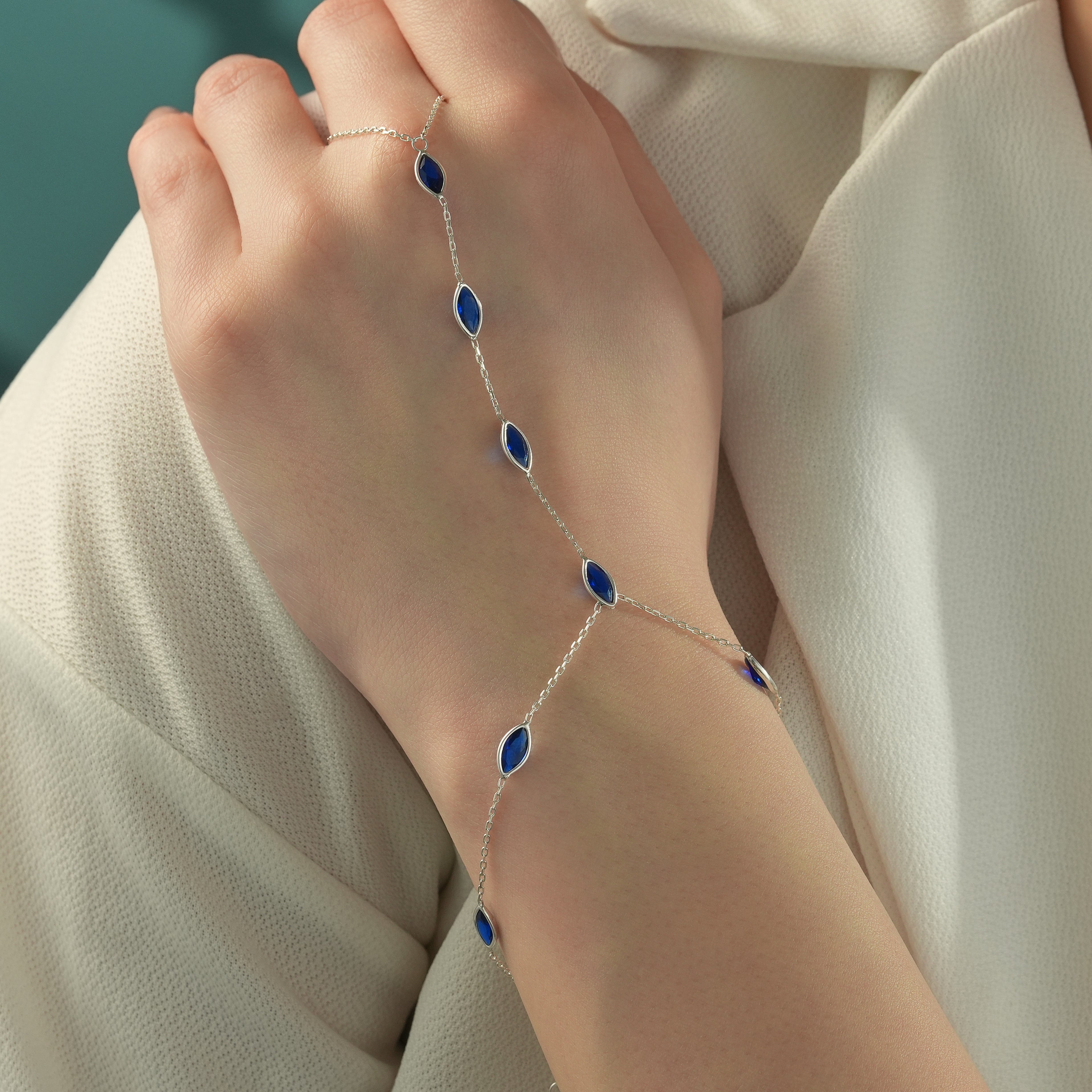 Woman wearing a 925 sterling silver hand chain bracelet featuring marquise-cut blue sapphire gemstones connected by a delicate finger-to-wrist chain.