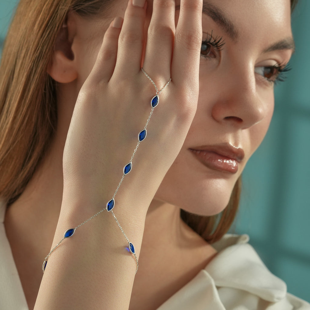 Woman wearing a 925 sterling silver hand chain bracelet with marquise-cut blue sapphire gemstones in an elegant finger bracelet design.