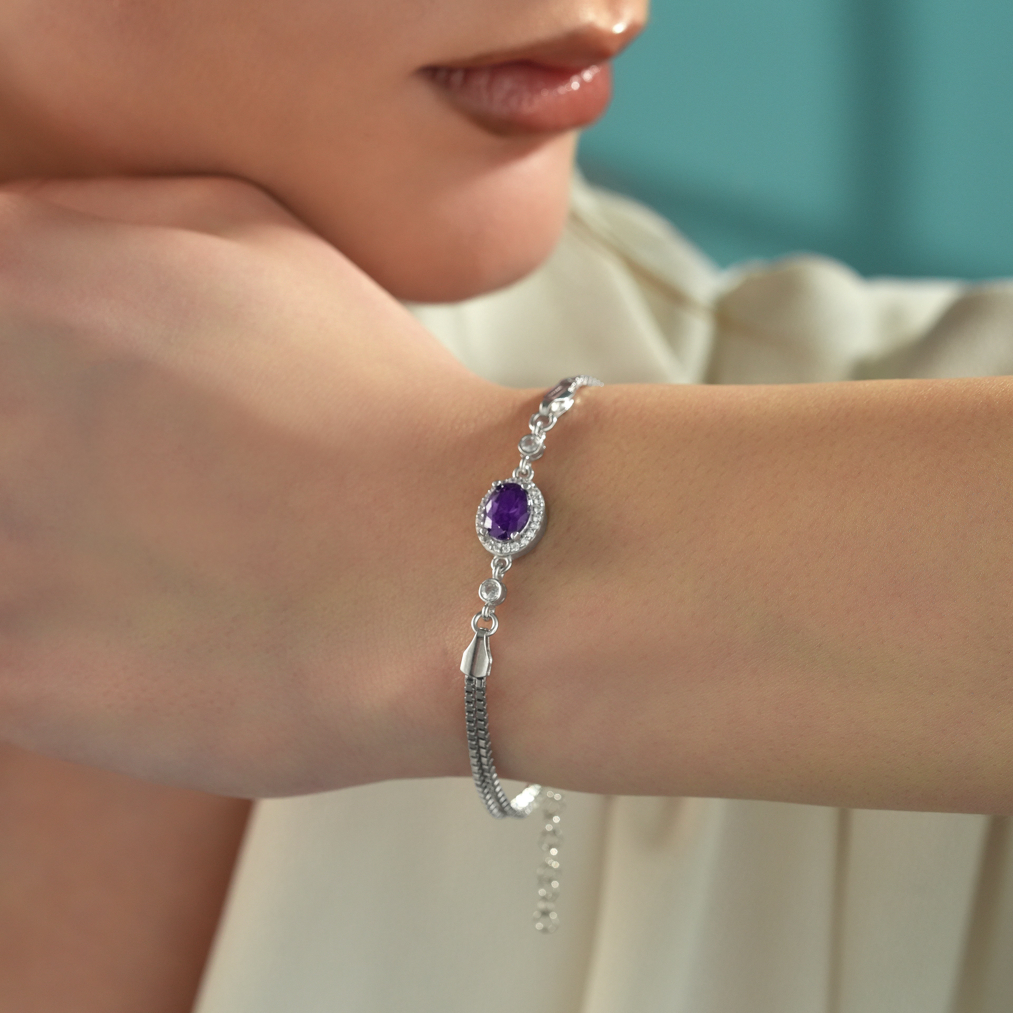 Woman wearing a 925 sterling silver bracelet with an oval amethyst color cubic zirconia centerpiece and adjustable box chain.
