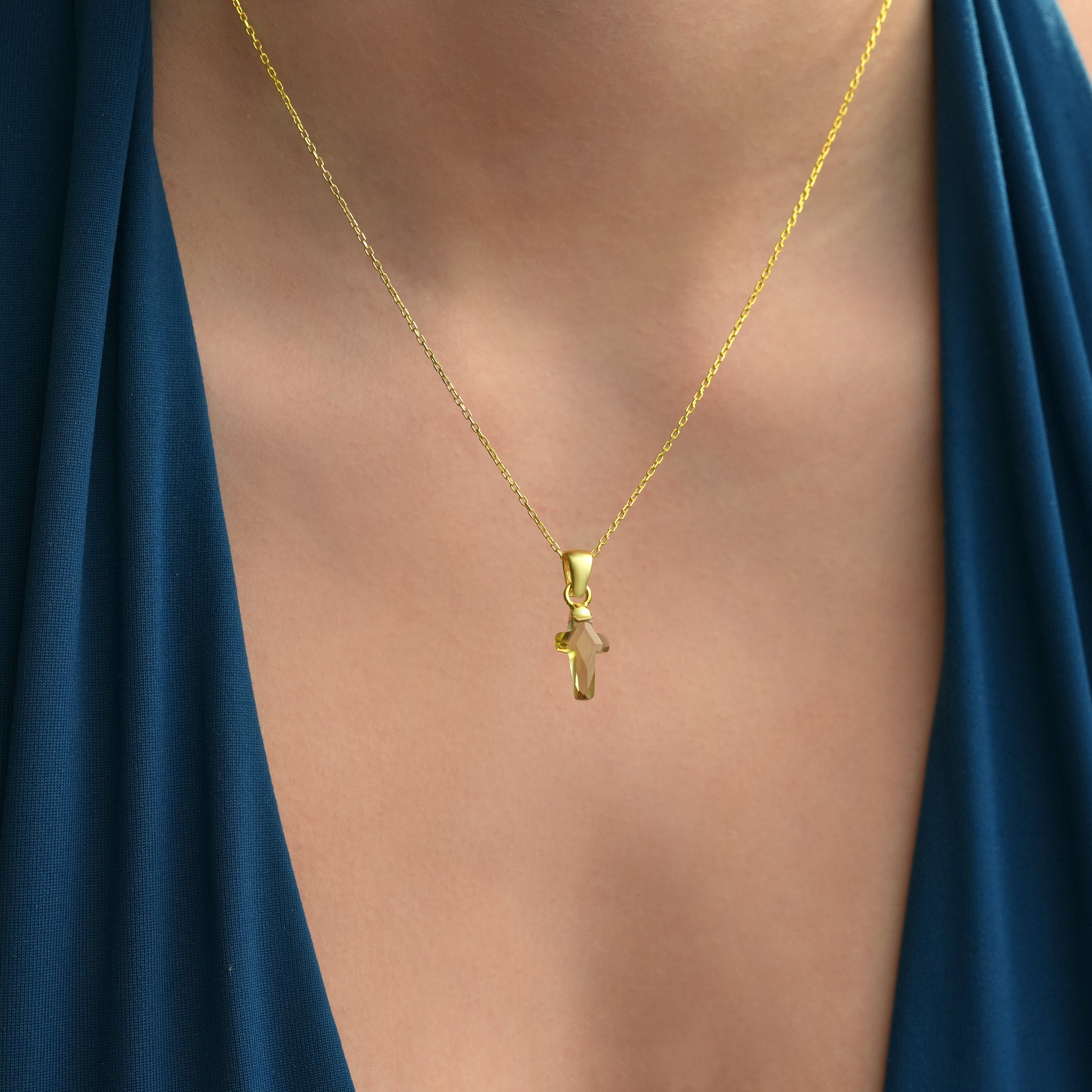 Close-up of a model wearing a 14K gold plated 925 sterling silver necklace with a natural color-changing diaspore cross pendant.