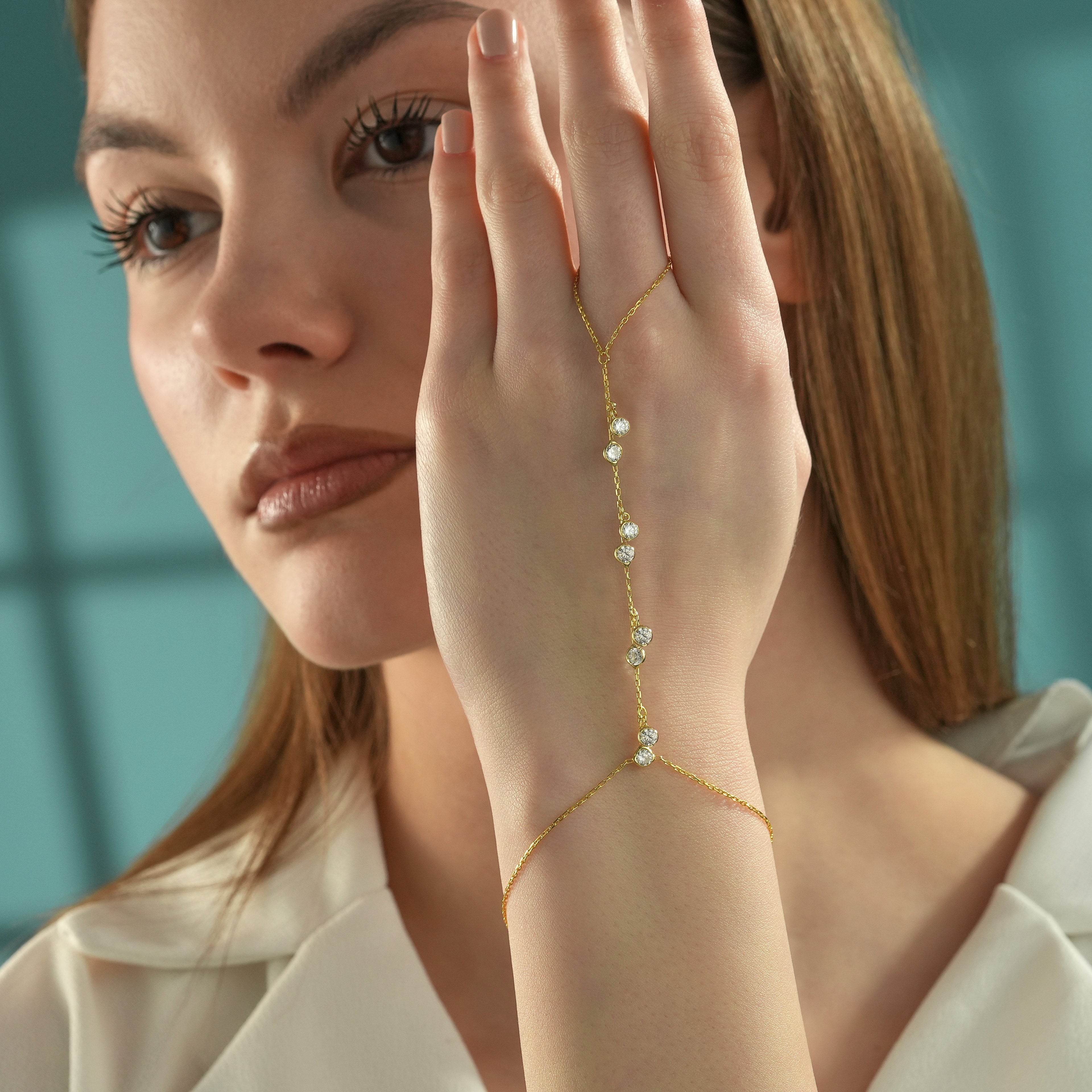 Woman wearing a 14K gold plated 925 sterling silver hand chain bracelet featuring dangling round clear cubic zirconia stones with a delicate ring-to-bracelet design.