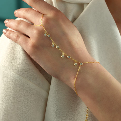 Close-up of a 14K gold plated 925 sterling silver hand chain bracelet featuring dangling round clear cubic zirconia accents on a delicate chain.