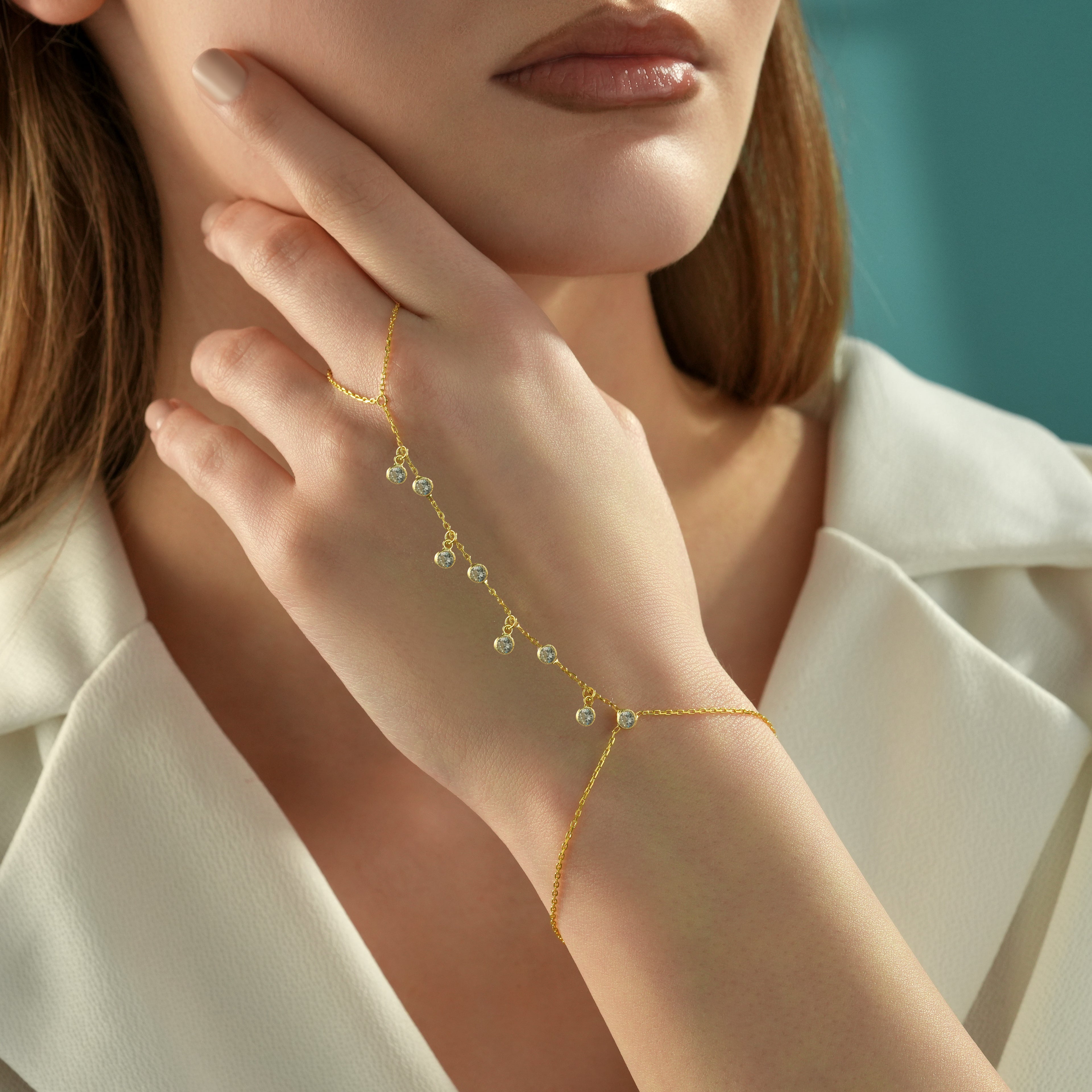 Woman wearing a minimalist 14K gold plated 925 sterling silver hand chain bracelet with dangling round clear cubic zirconia stones.
