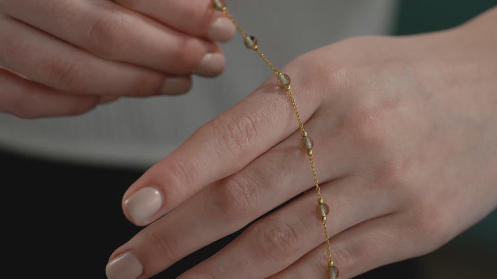 Close-Up Video Woman wearing a delicate 14K gold plated bracelet with faceted color changing gemstones and minimalist chain design.
