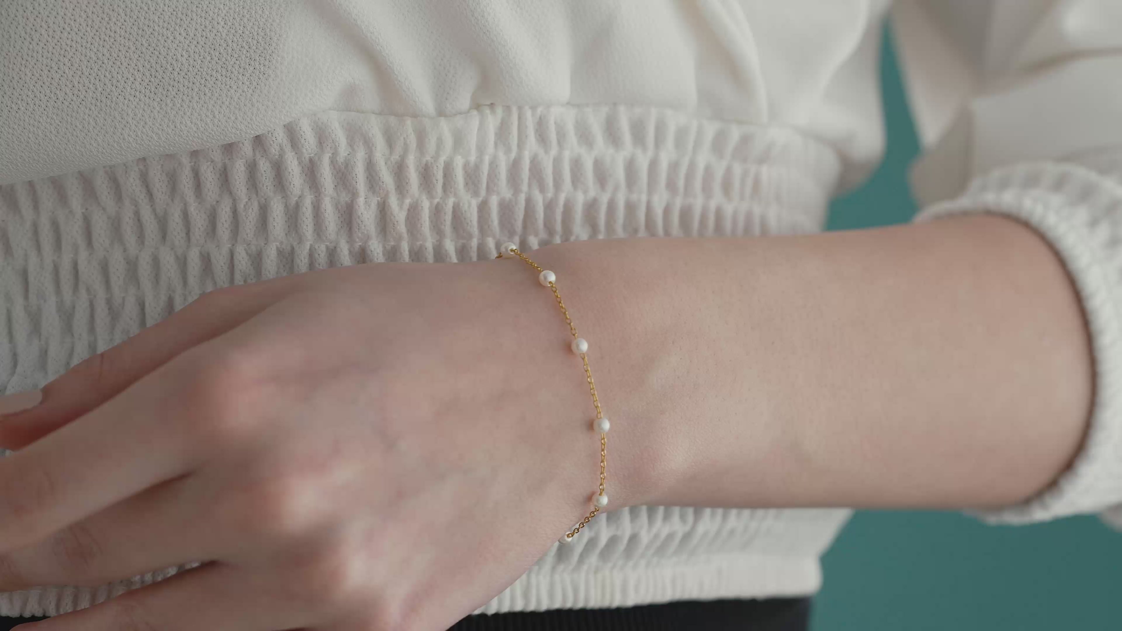 Video of Delicate 14K gold plated 925 sterling silver pearl bracelet featuring evenly spaced white pearls on a fine chain, worn on a woman's wrist.
